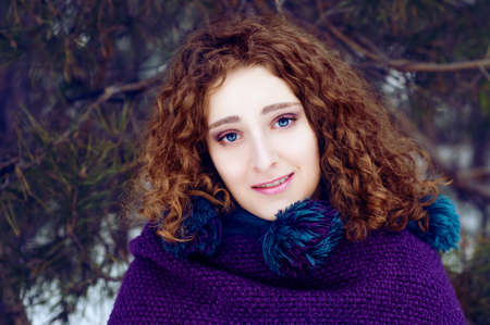 Mysterious young woman in purple knitted cape with a hood in winter forest smilingの写真素材
