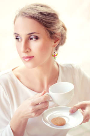 Beautiful elegant blonde sitting in a cafe drinking tea waiting for someone, shallow depth of field.の写真素材
