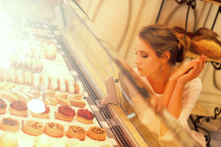 Woman choosing cakes and desserts in a cafe, sitting near the shop displayの写真素材