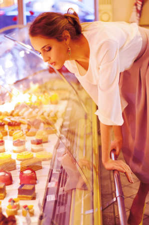 Woman choosing cakes and desserts in a cafe, sitting near the shop displayの写真素材