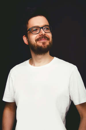 Young man with black hair and beard wearing glasses on black background
