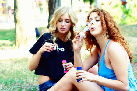 Two friends blowing soap bubbles and playing in the park. Summer activities.の写真素材