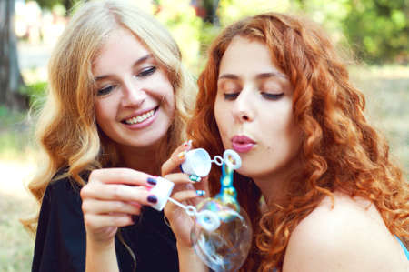 Two friends blowing soap bubbles and playing in the park. Summer activities.の写真素材