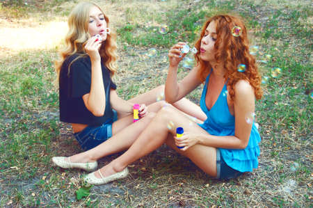 Two friends blowing soap bubbles and playing in the park. Summer activities.の写真素材