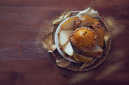 Caramelized pear dipped with chopped peanuts decorated with golden leavesの写真素材