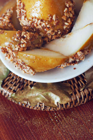 Caramelized pear dipped with chopped peanuts decorated with golden leavesの写真素材