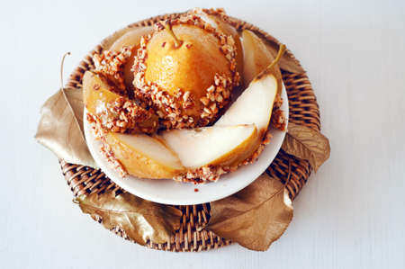 Caramelized pear dipped with chopped peanuts decorated with golden leavesの写真素材