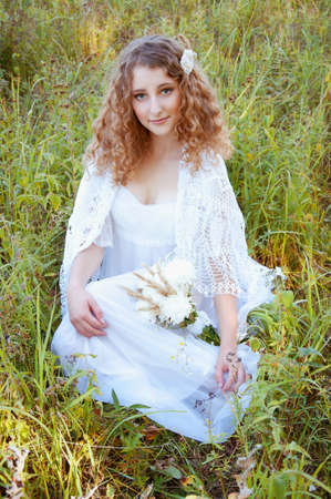 Woman with curly golden hair smiling standing in the field holding a bouquet of white flowersの写真素材