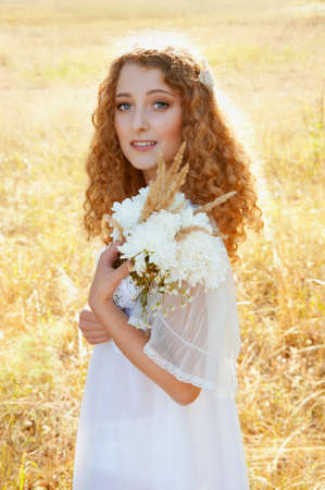 Woman with curly golden hair smiling standing in the field holding a bouquet of white flowersの写真素材