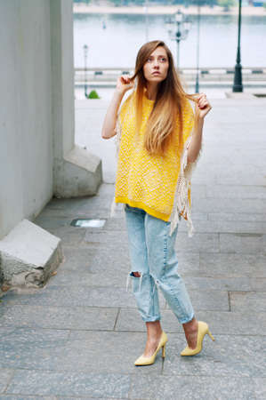Street city fashion redheaded girl with long hair wearing yellow poncho and boyfriend jeansの写真素材