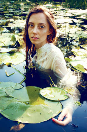 Tender young woman swimming in the pond among water lilies basking in the sun in shallow watersの写真素材