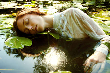 Tender young woman swimming in the pond among water lilies basking in the sun in shallow watersの写真素材