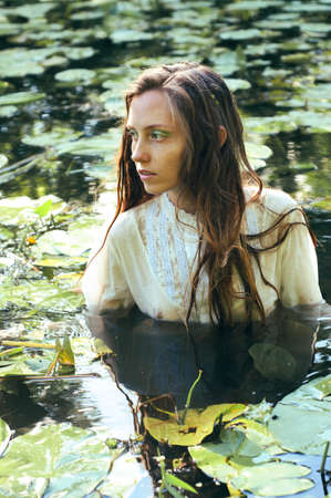 Tender young woman swimming in the pond among water lilies basking in the sun in shallow watersの写真素材