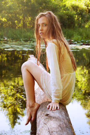 Redhead woman sitting on a tree bark near river in wet blouseの写真素材