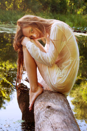Redhead woman sitting on a tree bark near river in wet blouseの写真素材