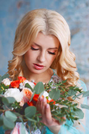 Charming young blond woman with curly hair holding fresh flowers bouquet with roses, carnations and eucalyptus leavesの写真素材