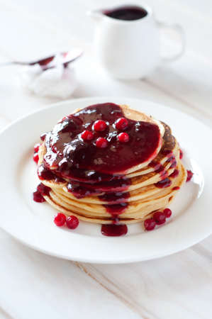 Light breakfast. Fresh pancakes on white plate with berry jam in morning light.