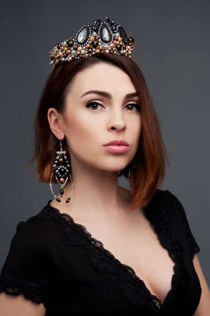 Sexy brunette in black dress with deep cleavage wearing beaded crown headpiece and earringsの写真素材