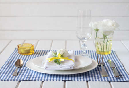 Table setting with blue checkered tablecloth, white napkin, silverware, yellow decoration and...