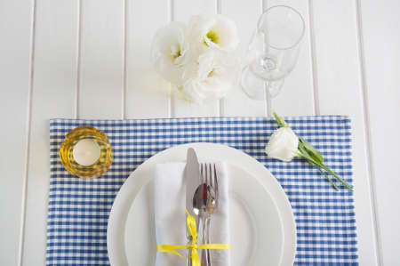 Table setting with blue checkered tablecloth, white napkin, silverware, yellow decoration and...