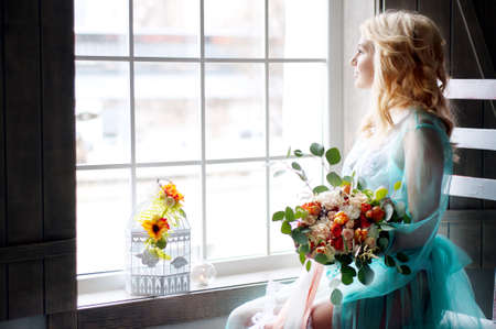 Bridal morning boudoir with smiling charming blond woman wearing mint transparent peignoir and holding fresh flowersの写真素材