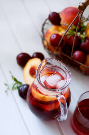 Iced fruit compote with peaches and plums. Cold summer drink with fruit in a basket in the back.