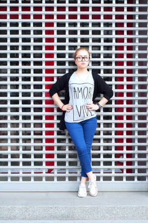 Young adult caucasian woman with blond hair tied in a bun in glasses wearing blue pants, tee-shirt...