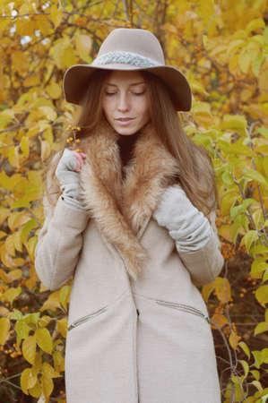 Retro look. Beautiful ash blond with freckles, long hair in fur collar coat and fedora hat outdoors in autumnの写真素材