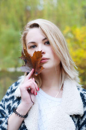 Cute smiling blond woman in black and white knitted warm cardigan strolling in autumn parkの写真素材