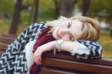 Cute smiling blond woman in black and white knitted warm cardigan relaxing  in autumn parkの写真素材
