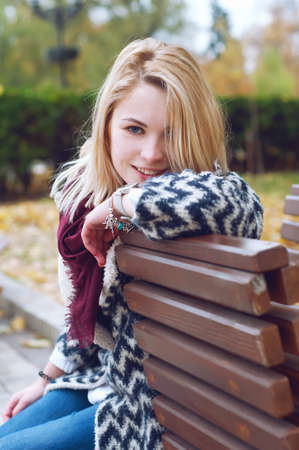 Cute smiling blond woman in black and white knitted warm cardigan relaxing  in autumn parkの写真素材