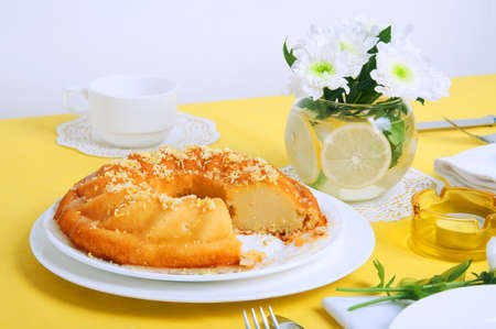 Yellow summer table setting with lemon bundt cake, white plates, teapot and chrysanthemum flowers in a glass vaseの写真素材