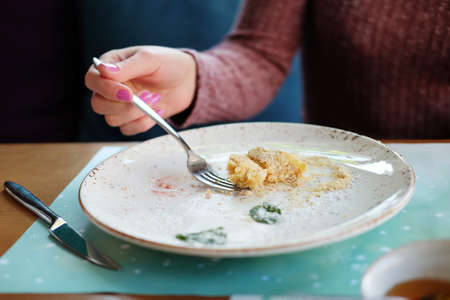 Woman eating a piece of napoleon cake dessert made of thin layers of pastry with custard filling sprinkled with sugar powder, mint leaves on a plateの写真素材
