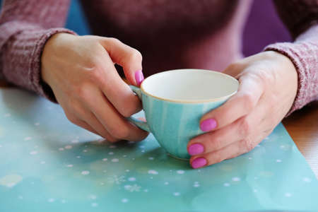 Woman drinking tea with honey holding cup with her hands sitting in restaurant. Hands closeup.