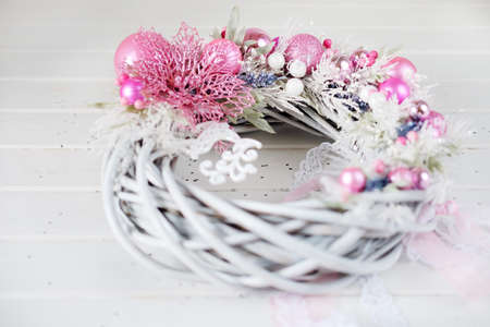 Christmas wreath winter holiday door decoration in white and pink with artificial flowers, glitter, christmas toys and white deer figure with lace ribbonsの写真素材
