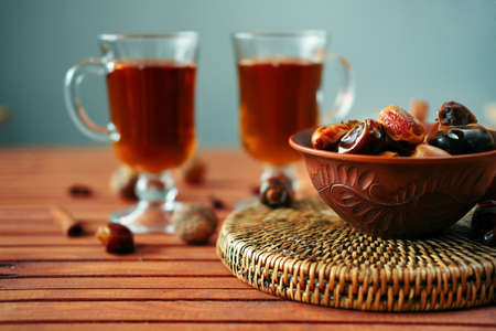 Bowl of dried dates and other spices on old wooden table with tea in glasses.の写真素材