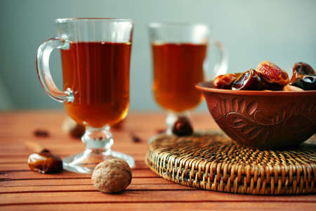 Bowl of dried dates and other spices on old wooden table with tea in glasses.の写真素材