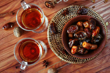 Bowl of dried dates and other spices on old wooden table with tea in glasses.の写真素材