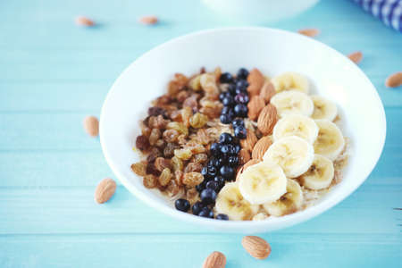Healthy breakfast. Oatmeal in a white bowl with banana, almond nuts, blueberries and raisins.