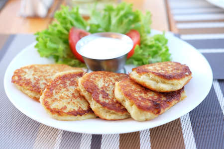 Potato pancakes served on plate with sour cream and salad leaves. Traditional Ukrainian and Russian cuisine.の写真素材
