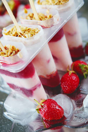Frozen yoghurt popsicles with strawberries and ice on silver plateの写真素材