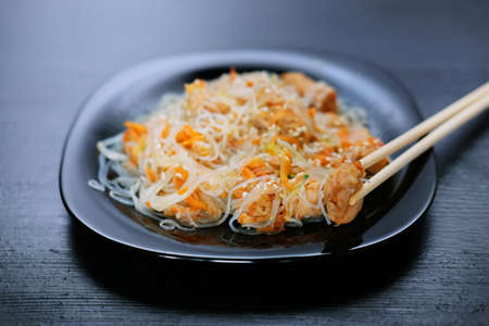 Asian traditional food. Fried rice noodles with chicken meat, vegetable slices sprinkled with sesame seeds.の写真素材