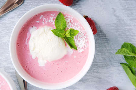 Cold creamy strawberry soup sprinkled with coconut chips with a scoop of ice cream and mint leaves....