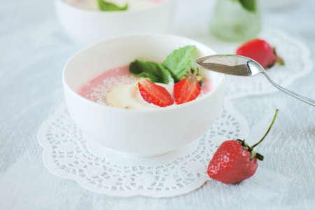Cold creamy strawberry soup sprinkled with coconut chips with a scoop of ice cream and mint leaves. Cold summer dessert.の写真素材