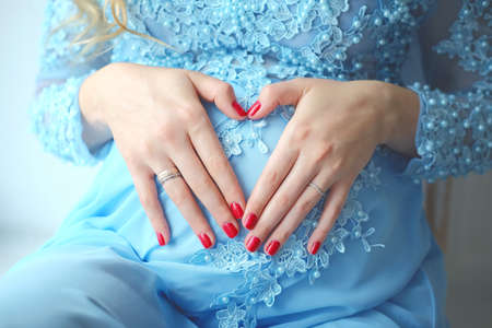 Pregnant woman in blue dress holding hands on her tummy inn the shape of heartの写真素材