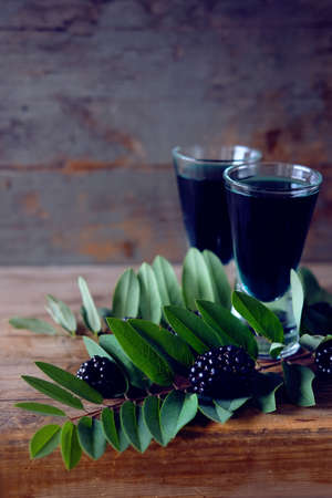 Blackberry fruit liqueur in two shot glasses with berries and green leaves. Strong local alcohol drinks.の写真素材