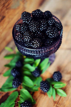 Blackberries on wooden backdrop in dark purple glass bowlの写真素材