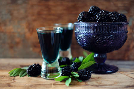Blackberry fruit liqueur in two shot glasses with berries and green leaves. Strong local alcohol drinks.の写真素材