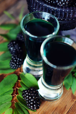 Blackberry fruit liqueur in two shot glasses with berries and green leaves. Strong local alcohol drinks.の写真素材