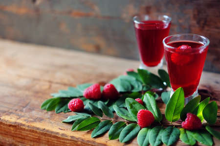 Raspberry fruit liqueur in two shot glasses with berries and green leaves. Strong local alcohol drinks.の写真素材